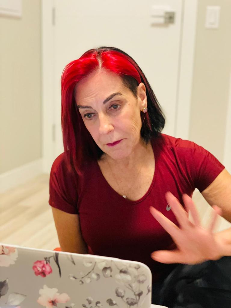 Dra. Elaine de Markondes conduzindo uma aula online de Pilates ao vivo, gesticulando enquanto explica aos alunos pelo notebook