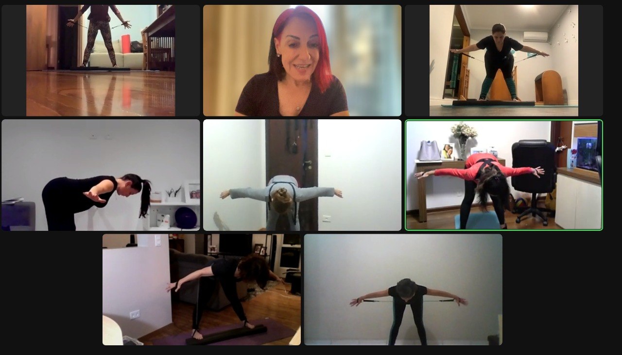 Tela do Zoom mostrando a Dra. Elaine conduzindo a aula com várias alunas executando posturas de Pilates ao vivo